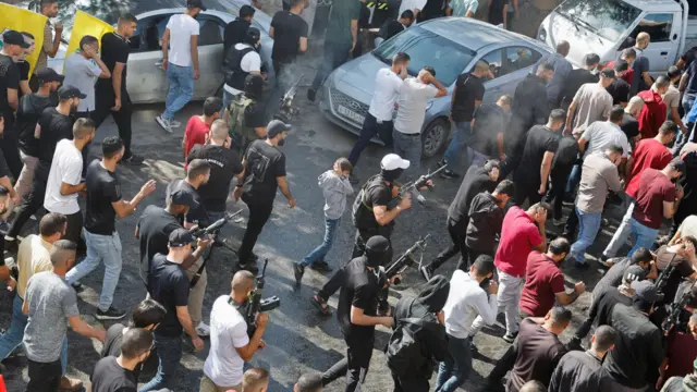 Men with guns attend the funeral of 11 Palestinians who were killed in an Israeli raid - 10 November 2023