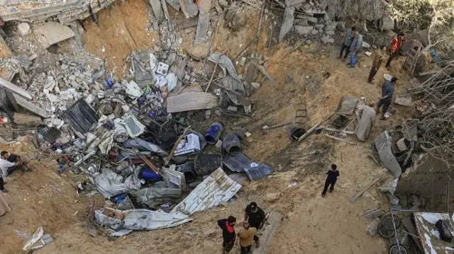 Palestinians stand at the edge of a crater following the Israeli bombardment of Rafah in the southern Gaza Strip