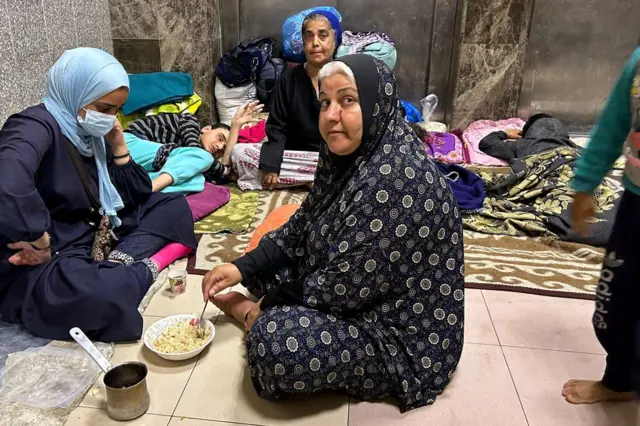 Women and children sit and lie on the floor of Al-Shifa hospital, some of them eating a meal