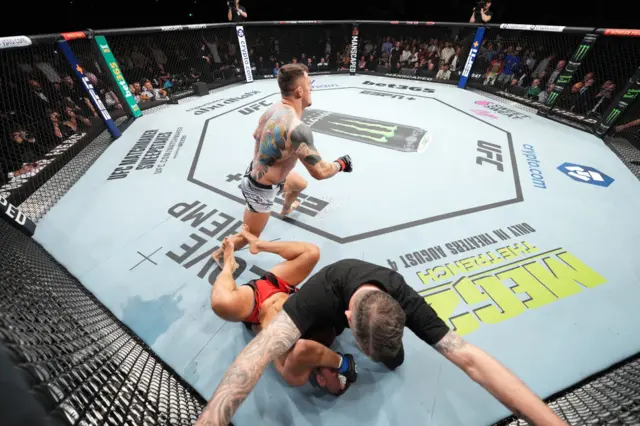Tom Aspinall runs away as referee Mark Goddard covers Marcin Tybura