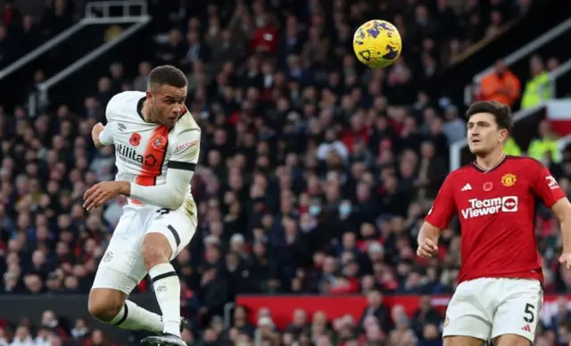 Carlton Morris heads the ball, Harry Maguire looks on