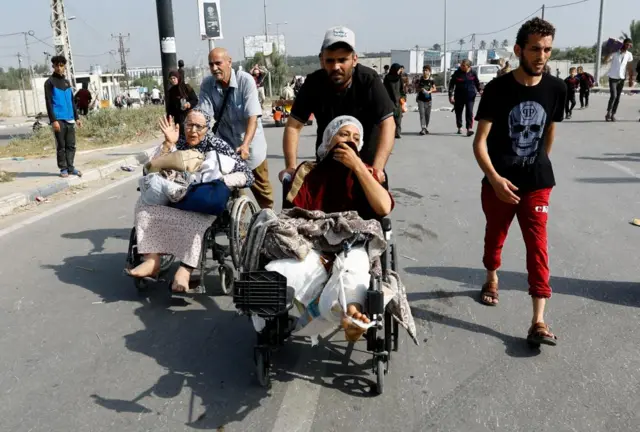 A Palestinian woman, who was injured in an Israeli strike and was staying at Al Shifa hospital, moves southward in a wheelchair after fleeing north Gaza