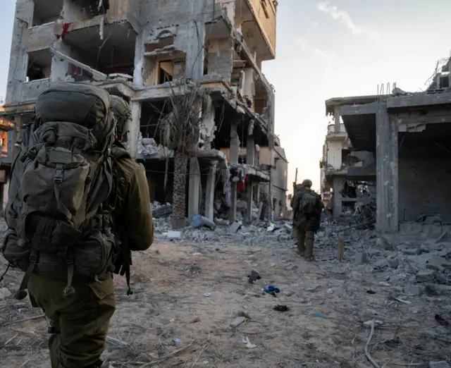 Israeli soldiers walk among destroyed buildings