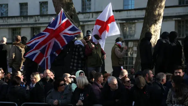 Protesters hold flags next to people attending the Armistice Day service