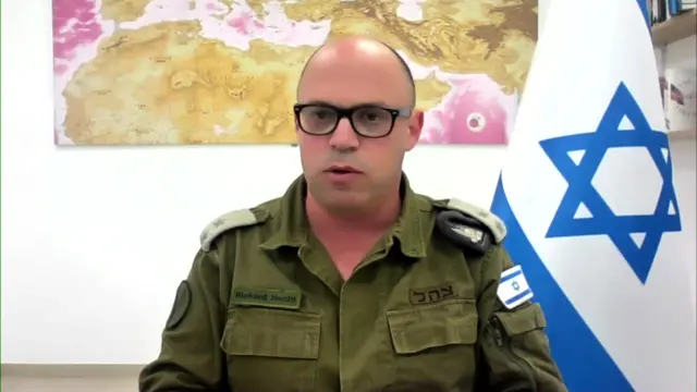 Lt Col Hecht speaks from an office. An Israeli flag hangs behind him