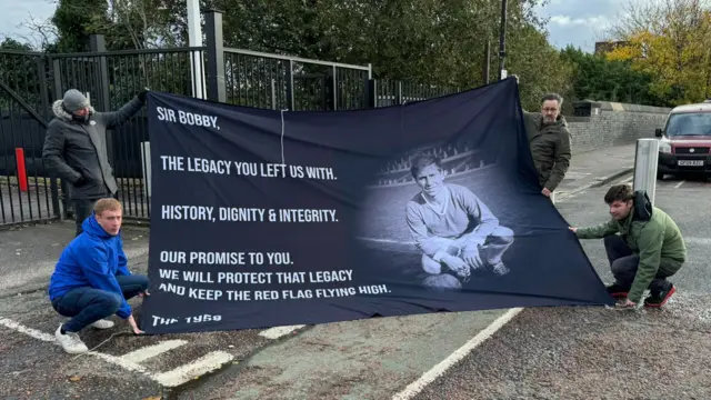 Fans holding a banner paying tribute to Sir Bobby at Old Trafford