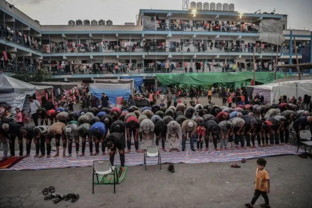 UNRWA school with washing and people on all the balconies and a group of men bending in prayer in the courtyard