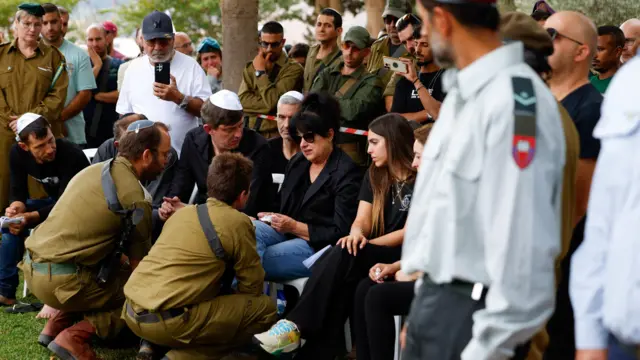 Soldiers crouch to talk to the mother of Sergey Shmerkin who is seated at the funeral