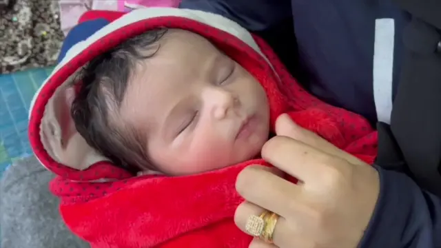 Newborn baby wrapped in red blanket, cradled in mother's arms