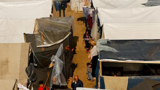 People walk at a tent camp sheltering displaced Palestinians