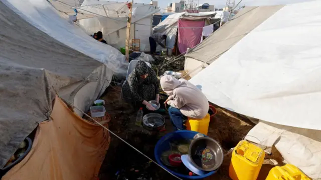 People cook at a tent camp sheltering displaced Palestinians