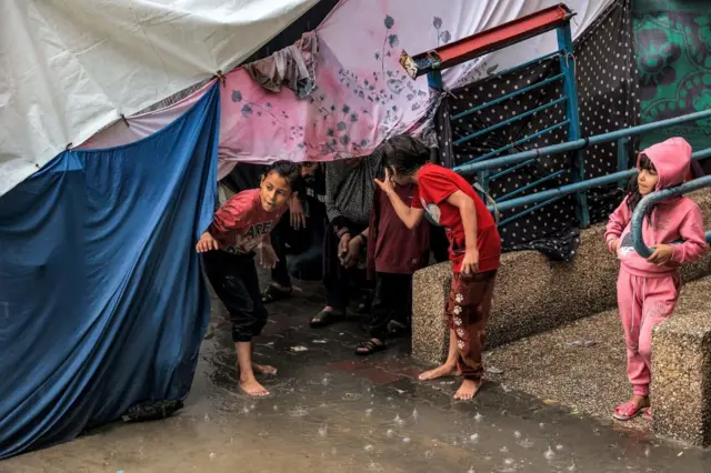 Children take shelter from the rain under a tent at a school in Rafah