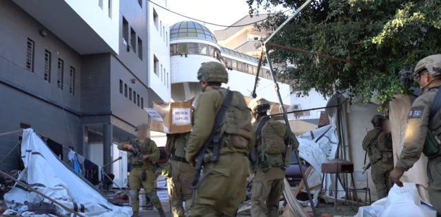 IDF soliders in the grounds of al-Shifa hospital. One is carrying a box marked "medical supplies"