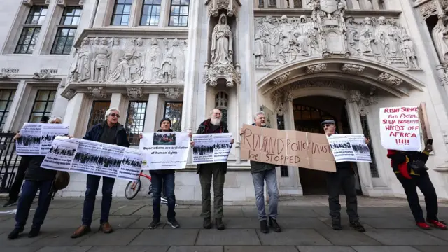 Demonstrators hold placards while protesting against the government's policy of sending asylum seekers to Rwanda, outside the Supreme Court of the United Kingdom in London, Britain, 15 November 2023.