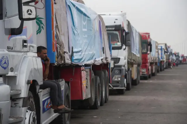 Trucks carrying humanitarian aid to Palestinians wait on the desert road on their way to the Rafah border crossing to enter Gaza