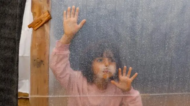 A young girl peers through the side of a tent as rain falls on Khan Younis