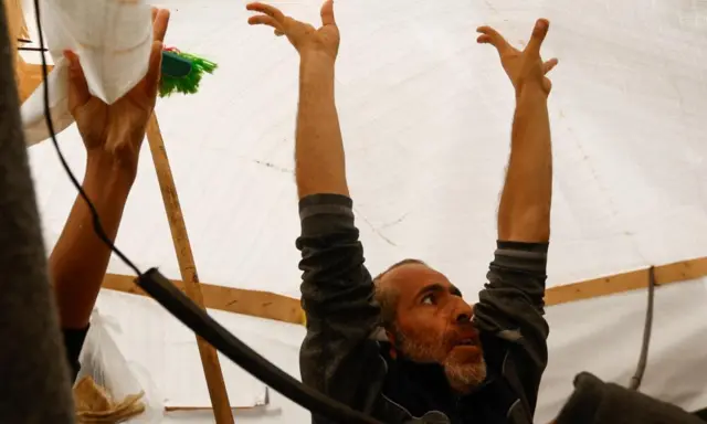 A man holds a white tent roof up with both hands