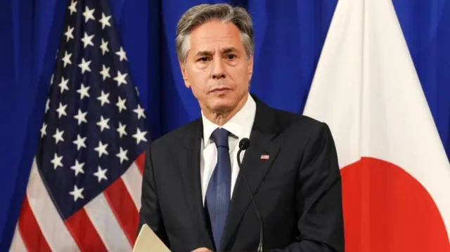 Blinken speaks at a lectern at the g7 - US and Japanese flags hang behind him