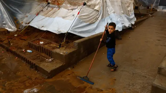 A boy who looks to be five years old mops a concrete path