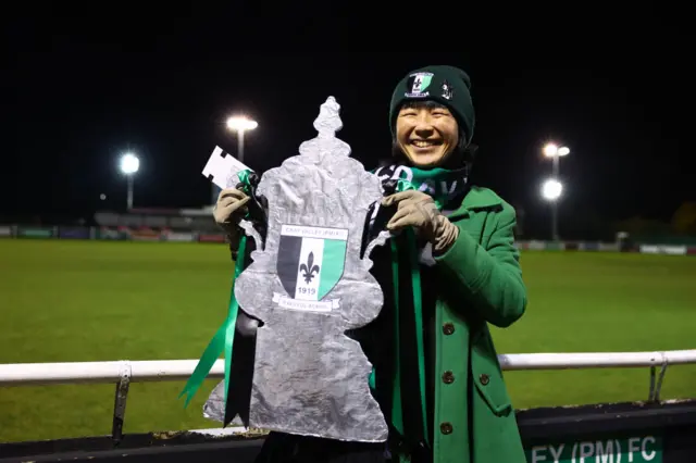 A Cray Valley Paper Mills fan poses for a photo whilst holding a tinfoil replica cut out of The FA Cup prior to the Emirates FA Cup First Round Replay match between Cray Valley Paper Mills and Charlton Athletic at Badgers Sports Ground