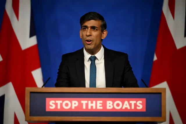 Rishi Sunak behind a lectern reading "Stop the boats"