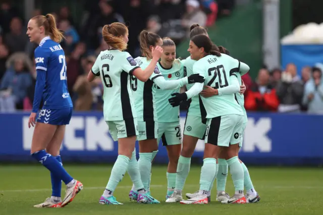 Chelsea players gather to celebrate a goal v Everton as an opponent trudges past in the foreground.