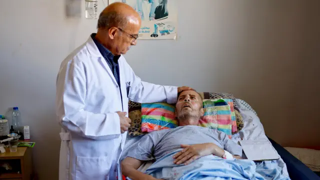 Cancer patient lies in hospital bed while doctor holds his head