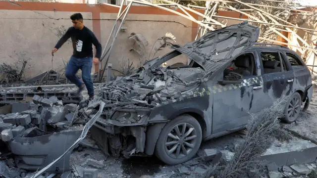 A Palestinian walks near a destroyed vehicle