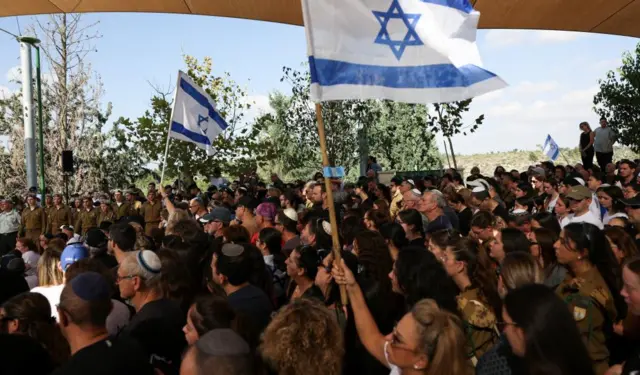 A crowd of people, some holding Israeli flags above their heads