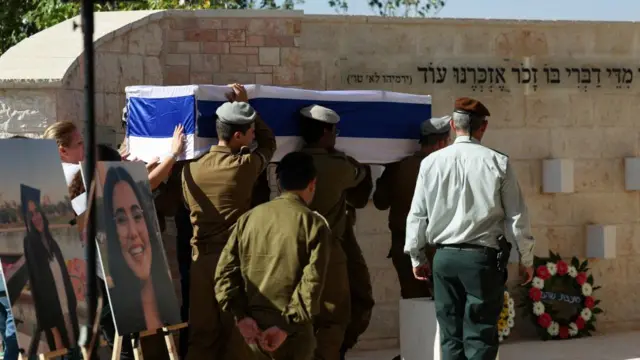 Soldiers carry a coffin draped in the Israeli flag. Nearby, photos of Marciano are displayed on easels