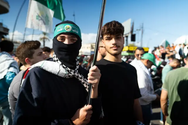 Two young men, one of whom is wearing a balaclava and holding a flagpole, attending a pro-Hamas rally