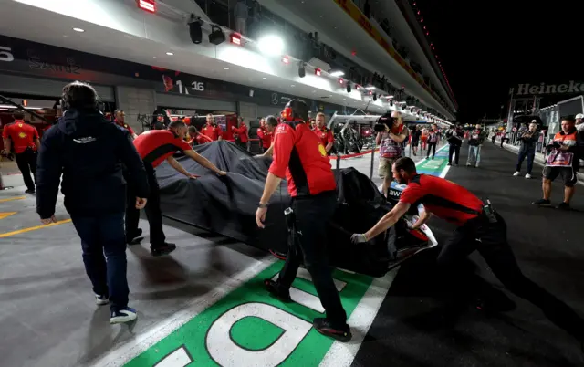 Carlos Sainz's damaged Ferrari is pushed back into the garage