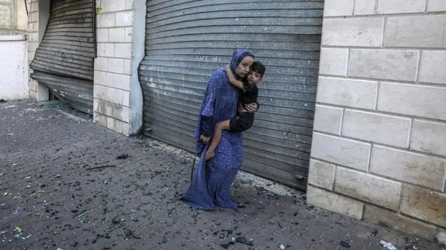 A woman carries her young son down a foothpath littered with debris