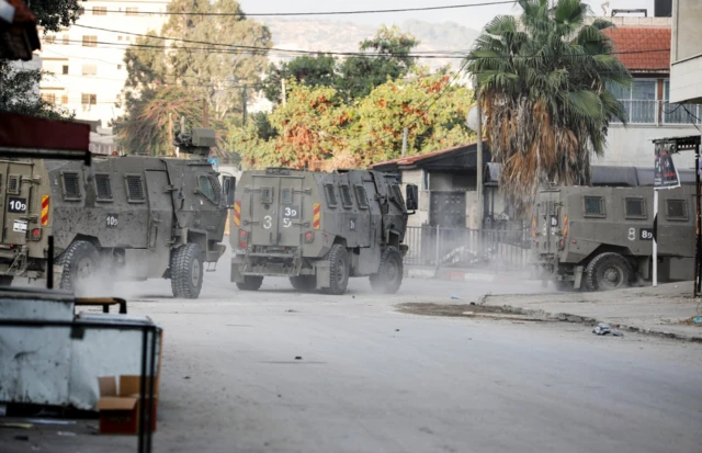 Israeli military vehicles move through a street after Israeli forces raided the Jenin refugee camp in the Israeli-occupied West Bankö 17 November 2023