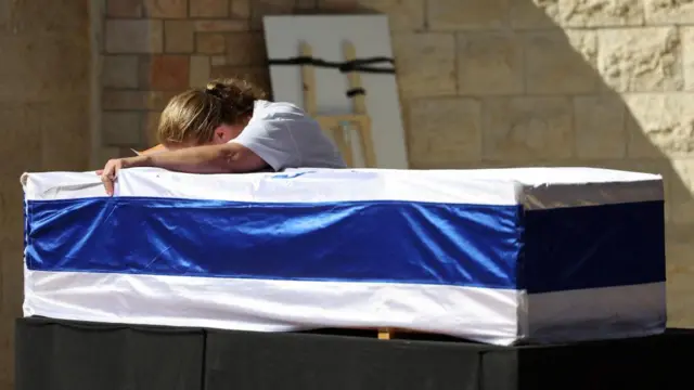 A woman is hunched over a coffin draped in the Israeli flag