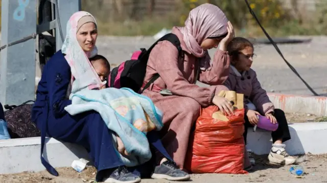 Two women sat on a curb with a baby and a child