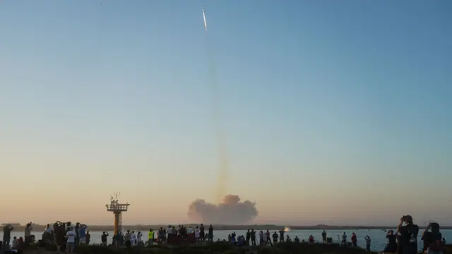 A sizeable group of people watch the rocket lift off - many through binoculars - just after 07:00 local tie (13:00 GMT)