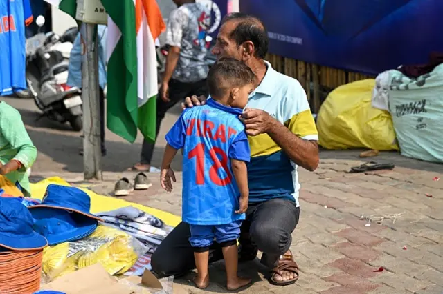 A father tries an India's cricket team jersey on his child at a stall outside the Narendra Modi Stadium in Ahmedabad