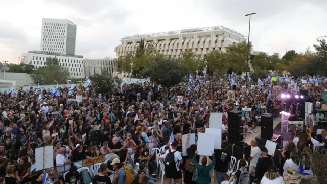 A crowd of people outside the prime minister's office in jerusalem, holding signs and Israeli flags