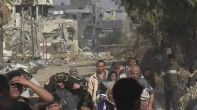 A group of people walk past ruin and rubble