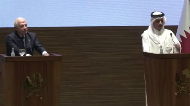 Borrell and Thani stand at lecterns on a stage