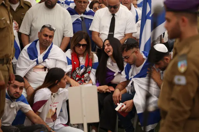 People crying and looking anguished. They have Israel flags around their shoulders