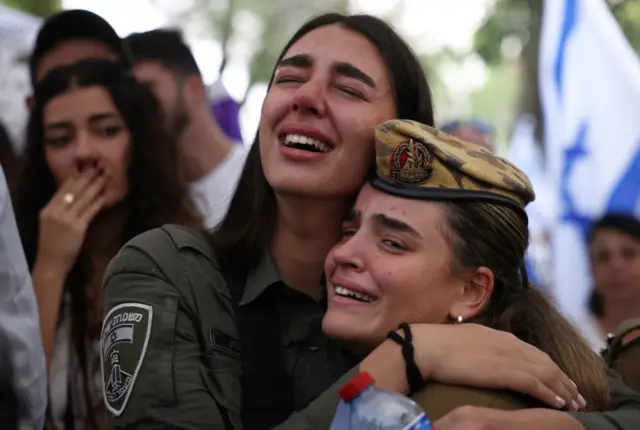 Two women, both in military uniforms, embrace and cry