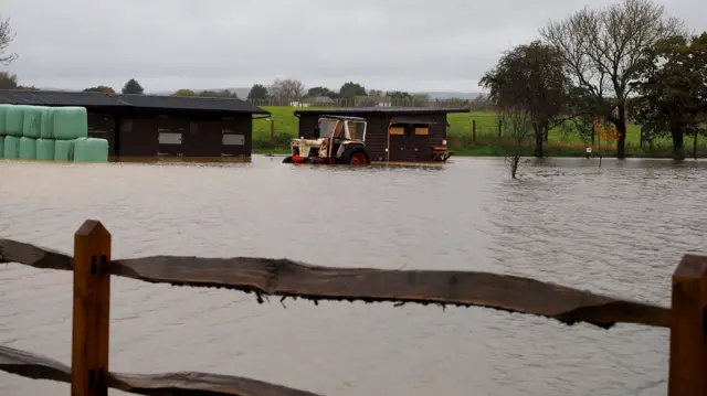 A flooded field in West Sussex. A tractor and barns are seen in the back of the image submerged in by water