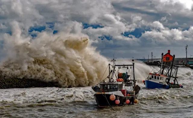 Fishing trawlers as waves crash against the harbour wall during Storm Ciaran in Folkestone, Kent,