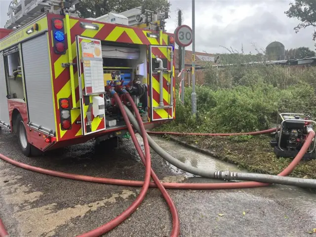 Firecrew has pumps running from a fire engine into flooded areas