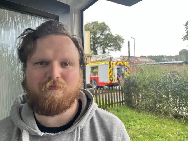 Dean Millward in the doorway of his home with a fire engine in the background