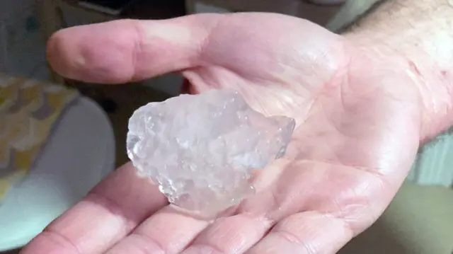 A large hailstone - larger than a golf ball - in the palm of a hand