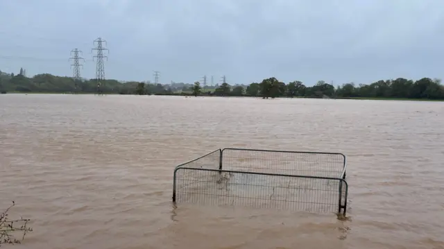 Flood water covers a large field. The tops of metal gates can be seen as water has submerged the rest