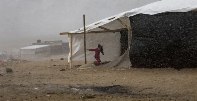 A youngster takes shelter from the rain at a temporary camp provided by the United Nations Development Program for displaced Palestinians who lost their homes in Israeli raids, in Khan Yunis, 19 November 2023